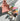 Sojourn Burst Elements Ritual Set, featuring a terracotte coloured drawstring pouch embossed with 'Sojourn' and ‘Burst Your Energy,’ a small energy spray labeled ‘Ich Tanke Energie,’  a colourful Sojourn ritual card and six rough and polished gemstones - green aventurine, citrine, smokey quartz - with a person listening to music, arranged together on a flat sunlit surface on a neutral background.