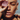Close‑up of a freckled face in bright sunlight holding a rough pink gemstone crystal over one eye, with a gold hoop earring and a softly blurred outdoor background.